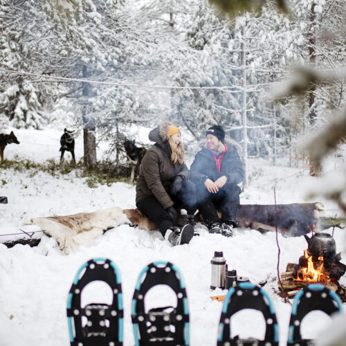 Two women talking and laughing beside a fire in Finnish Lapland after snowshoeing