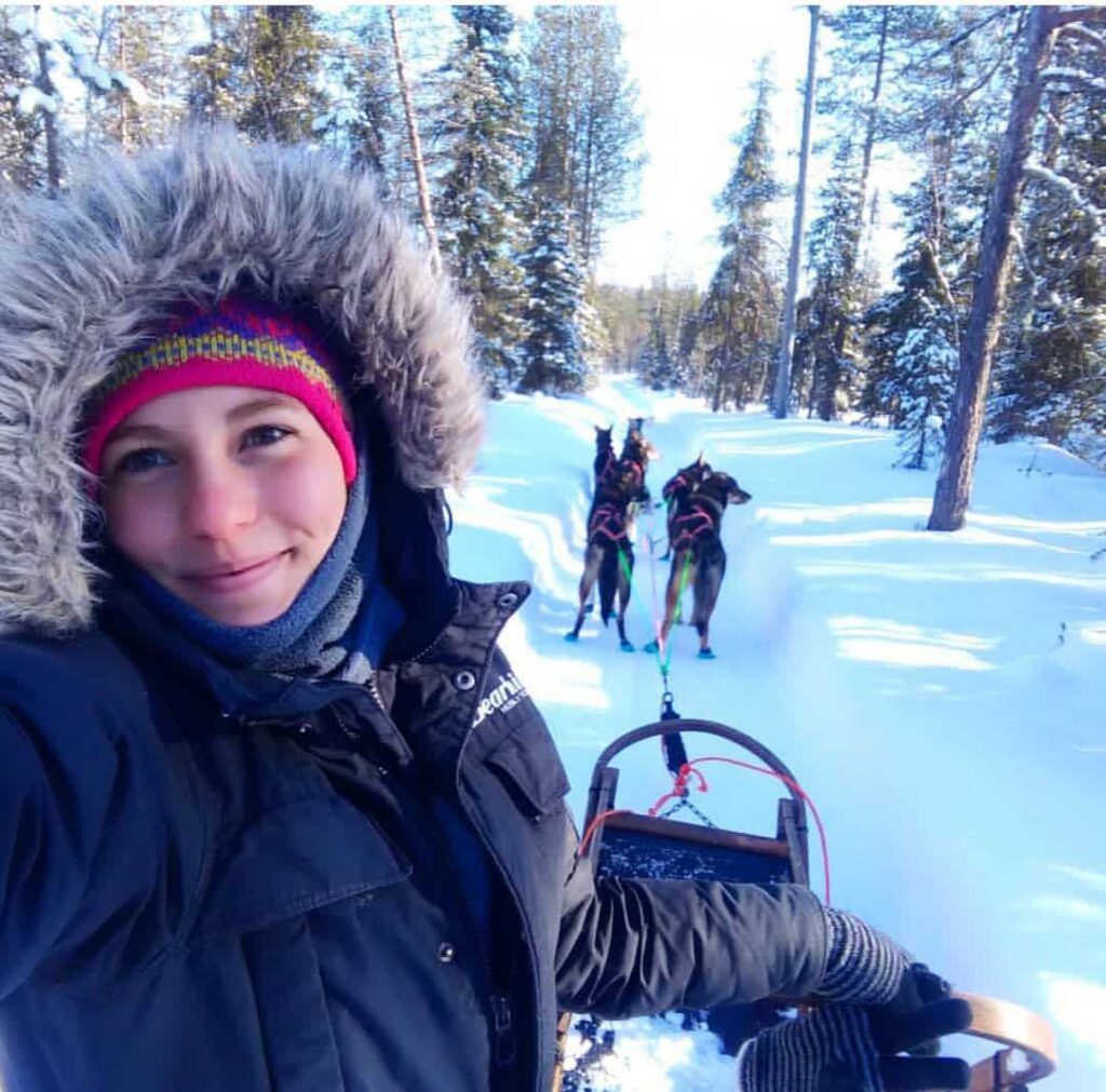Cristina driving a team of dogs through the snowy forest