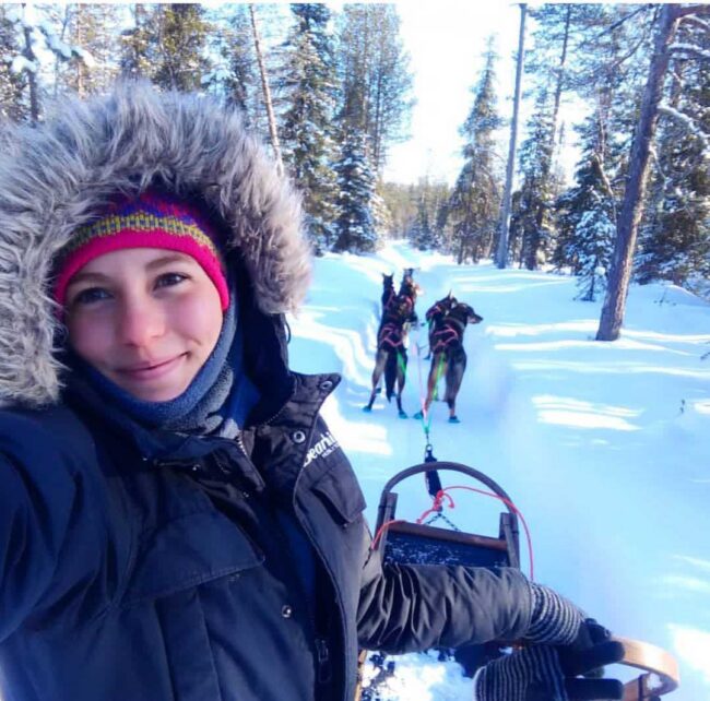 Cristina driving a team of dogs through the snowy forest